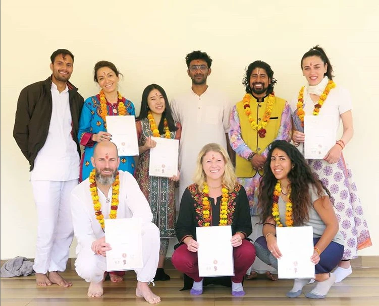 A group of yoga teacher training graduates in flower garlands holding certificates